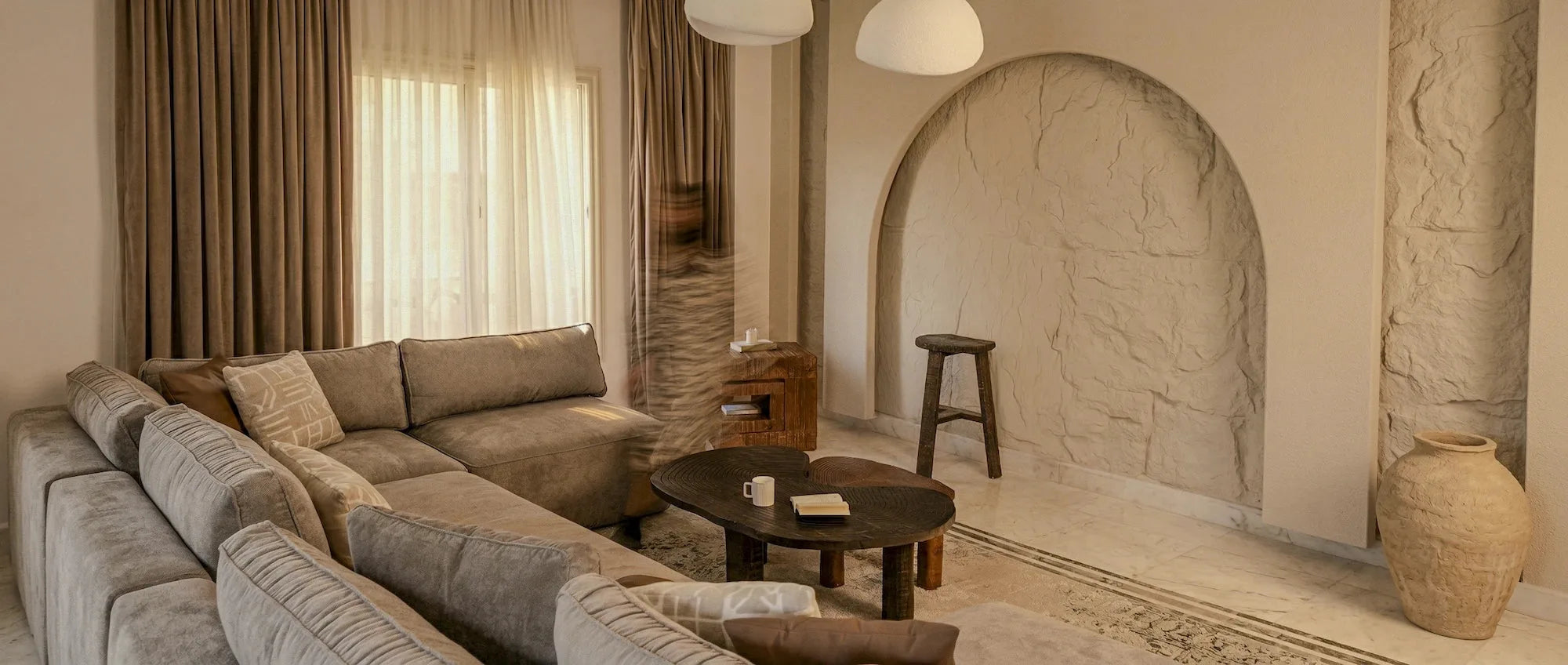 Warm minimalist living room with arched stone niche, curved sofa, and natural wood accents